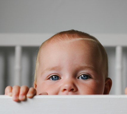 Bébé regardant par-dessus la barrière d’un berceau, illustrant les nourrissons pouvant être vulnérables au virus respiratoire syncytial (VRS).